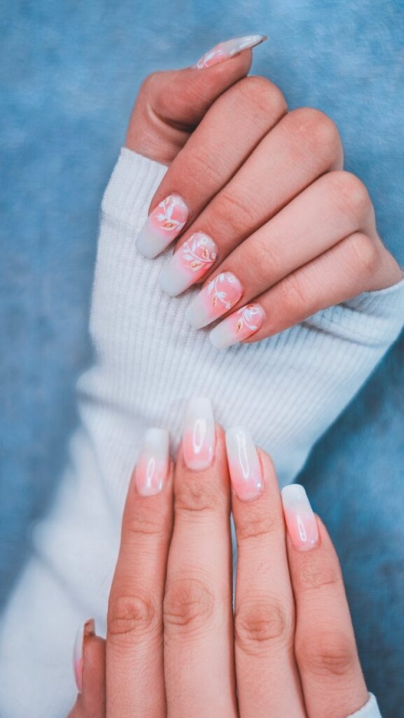 Close-up of hands showcasing elegant gradient nail art with floral designs.